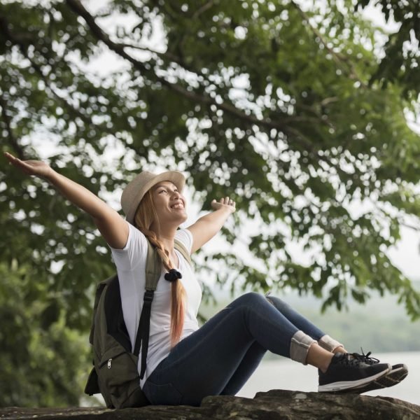 Young happy woman sitting with backpack enjoy the nature after hike. Woman travel concept.